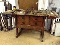 Front view of wooden workbench with 4 drawers and various hand tools on top, including a mounted Columbian Hardware vise on the left side.