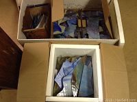 Four small boxes filled with assorted stained glass pieces showing a mix of blues and greens with varied textures and an additional box likely containing metal frames.