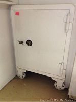 Front full view of large white Yale safe with caster wheels, closed door, paint chips visible
