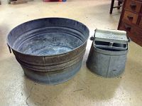 Photo showing large Wheeling galvanized tub next to vintage De Luxe roller top bucket on concrete floor