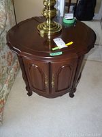 Front angle view of one table showing round top, scalloped edge, double doors and carved feet.