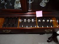Open wooden drawer displaying a variety of silver plated cutlery utensils such as forks, spoons, and knives.