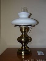 Full view of one hurricane lamp showing brass base, white glass shade, and clear glass chimney.
