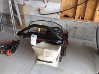 Front view of mower with folded handlebars and attached grass bag