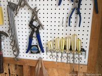 Photo of combination wrenches, locking pliers, screwdrivers, and measuring tape hung on pegboard.