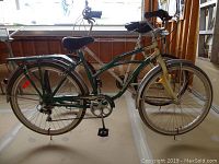 Left side view of green and cream cruiser bicycle showing frame, saddle, rear rack and rear fender