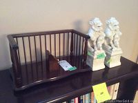 Photo showing two white ceramic Foo Dogs and wooden display stand positioned on a bookshelf.