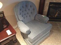 Light blue chenille swivel rocker chair shown from an angle with tufted back and padded arms.