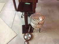Photo of dark wood plant stand, woven sewing basket, and round wooden barometer on the floor.