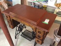 Full view of the treadle sewing machine desk with dark reddish-brown painted top and ornate cast iron legs.