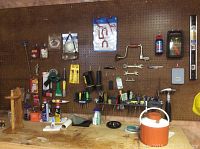 Wide view of pegboard and workbench with assorted multi-type handyman tools and supplies organized and displayed