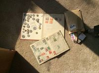 Full view of two open stamp albums, assorted loose coins placed on one album page, and a brown paper bag with loose stamps spilling out.
