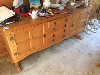 Side view showing full length of wooden sideboard with four drawers and two doors, surface holding various household items.