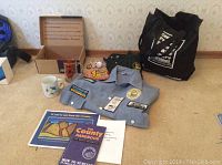 Photo showing light blue golf shirt with patches, two reusable black tote bags, various books and pamphlets, mugs, pins, and accessories spread on beige carpet.