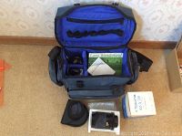Top view of opened camera bag showing internal padded compartments, Tokina 70-210mm lens, lens hood, booklets and lens packaging box.