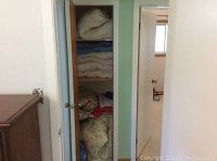 View inside closet showing multiple shelves filled with folded comforters, pillows and linens in a stacked arrangement.