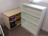 Photo of the white book shelf next to the storage cabinet with colorful sliding bins, showing overall size and condition.