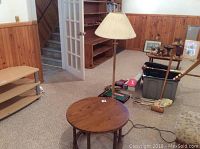 View of the small circular wooden table and standing floor lamp in the room with wood-paneled walls