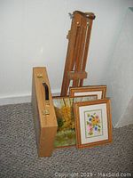 Small wooden folding easel, two small framed paintings, oil on board painting leaning against wall next to a wooden artist box
