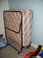 Side view of the folding bed standing upright on wheels with striped fabric mattress.