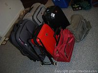 Photo showing seven pieces of luggage and bags arranged on carpeted floor including hard and fabric bags.