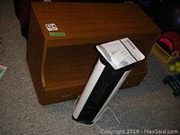 Noma ceramic tower heater on or near wooden stand on carpeted floor, heater cord visible, instruction manual on top.