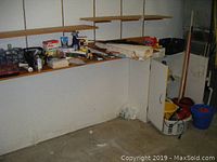 Wide view of melamine cabinet with various cleaning supplies, tools, wallpaper roll, mop buckets and brooms on and around it.