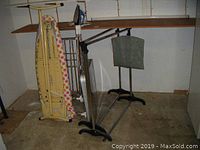 Photo showing two extendable metal clothing racks and vintage ironing board leaning against wall.