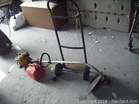 Photo of hand cart lying on its side with weed trimmer and fuel can next to it, showing overall condition and items included.