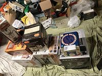 Photo showing multiple boxed kitchen appliances including Keurig coffee maker, Melitta coffee maker, George Foreman cooker, Pro Logic Dutch oven, and others on green cloth.