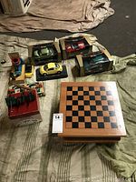 Overview of boxed and unboxed model cars, wooden chess board, small plastic cannons, card shuffler, and backgammon set.