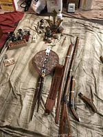 Photo showing a range of indigenous weapons and artifacts including shields, spears, rifle, swords, with Asian samurai statue and brass pipes in the background.