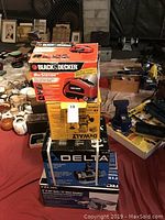 Stack of four boxed electric tools including Black & Decker Air Station on top, DeWalt box, Delta bench grinder box, ROK belt/disc sander box