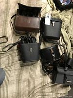 Five binoculars in cases arranged on striped fabric
