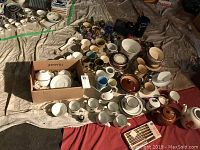 Overall assortment of ceramic mugs, bowls, teapots, and canisters laid out on floor