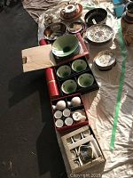 Photo showing a variety of bowls, plates, teapots, teacups, some in boxes and some arranged on cloth.