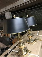 Pair of brass pineapple table lamps with black shades on cardboard surface