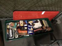 Green plastic tub filled with assorted tools and tool accessories, some packaged