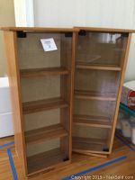 Two wooden media cabinets with glass doors shown side by side, doors closed, showcasing size and exterior.