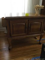 Front exterior view of the brown wooden Queen Anne style cabinet showing two paneled doors and curved legs.
