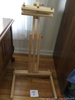 Front view of wooden adjustable floor stand showing base, vertical supports, wing nut adjustment points, and top clamp area.