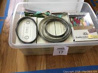 Plastic bin filled with over 25 boxes of DMC embroidery thread skeins, with embroidery hoops and pattern booklets on top