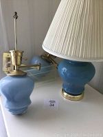 Photo showing one of the light blue ginger jar swing arm wall lamps with brass fixture and base, next to the light blue ginger jar table lamp with white pleated shade.