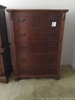 Front view of the Raymour & Flanigan highboy chest showing five drawers with ornate metal handles and carved vertical corner trim.