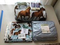 Photo of horse print fleece fabric blanket material with blue twin sheets and blanket binding fabric packages on top.