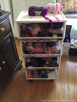 White plastic wheeled container with multiple drawers filled with yarn skeins and balls on hardwood floor near window and furniture.