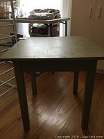 Front view of square wooden table showing four legs and top surface with visible wear.