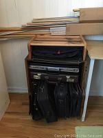 Wooden shelf holding multiple briefcases and computer cases stacked vertically and horizontally.