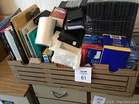 Photo showing a wooden crate filled with assorted office supplies such as clipboards, envelopes, various papers, protective sleeves, and storage cases.