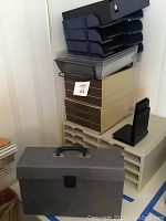 Stacked paper storage items including two sets of stackable drawer units, black metal bookends, portable file box, and black and clear plastic stacking trays.